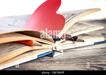 Libro e segnalibro a forma di cuore su tavolo di legno. Foto Stock