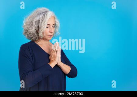 Donna matura che prega con mani piegate e occhi chiusi Foto Stock