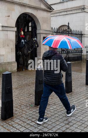 Whitehall, Westminster, Londra, Regno Unito. 8th Jan, 2023. Forti piogge hanno colpito le zone turistiche di Westminster con poche persone per strada. Guardia montata a Horse Guards con persona che passa con un ombrello Foto Stock