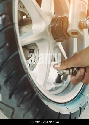 Mani di un uomo controllare la pressione del generatore di gas e gonfiare uno pneumatico su una motocicletta con un compressore pneumatico. Man controllo della pressione dell'aria e riempimento della pressione dei pneumatici Foto Stock