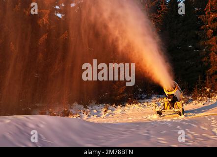 Snowmaker che produce neve in una stazione sciistica. Snowjet in luce laterale e con sfondo scuro al tramonto Foto Stock