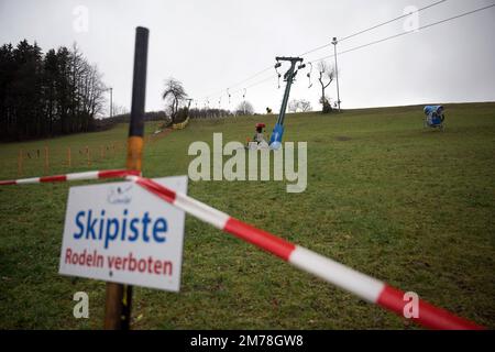 Gersfeld, Germania. 08th Jan, 2023. Un nastro barriera con l'indicazione "piste da sci - slittino proibito" è appeso vicino allo skilift di Zuckerfeld. La mancanza di neve e le temperature miti impediscono attualmente il divertimento sulle piste delle stazioni sciistiche dell'Assia. Credit: Sebastian Gollnow/dpa/Alamy Live News Foto Stock