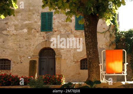 Sedia arancione in una tranquilla piazza nel borgo medievale tuscaniano di Monticchiello, Val d'Orcia, Toscana, Italia Foto Stock