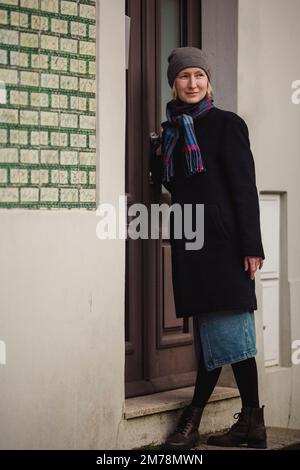 Una donna sul portico di una casa bussa alla porta. Foto Stock