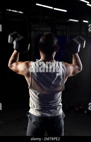 immagine verticale di un uomo muscoloso dalla schiena, premendo con un paio di manubri Foto Stock