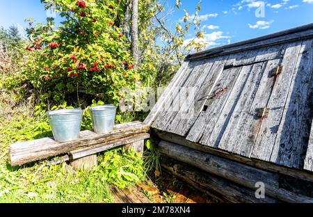 Secchi in metallo con acqua su una panca vicino a un villaggio di legno bene in una giornata di sole in campagna Foto Stock