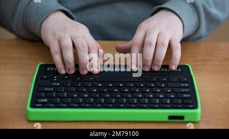 Un uomo cieco utilizza un computer con un display Braille e una tastiera per computer. Dispositivo incluso. Foto Stock