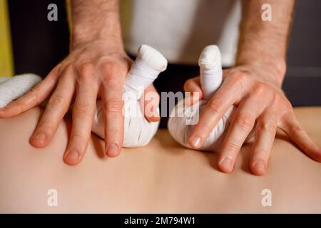 Сlose su donna che riceve massaggio alla schiena con borse di erbe nel salone termale Foto Stock