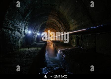 Tunnel fognario urbano a volta con acque reflue sporche. Foto Stock