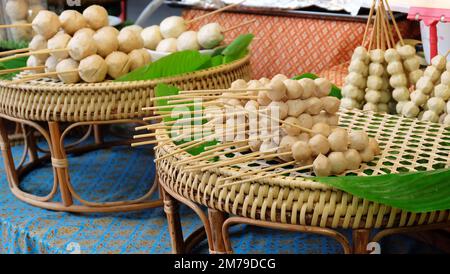 Spiedini con palle di pesce crudo impilati insieme, posti sopra un vassoio intrecciato, pronti per essere cotti. Foto Stock