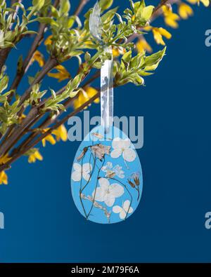 Legno compensato grezzo a forma di uovo di Pasqua blu decorato con fiori secchi pressati. Foto Stock