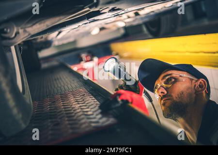 Controllo meccanico professionale del carro con una torcia durante l'appuntamento di ispezione programmata del veicolo presso la stazione dell'automobile. Foto Stock