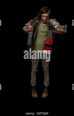 Uomo con pullover in lana colorata e pantaloni grigi con grandi stivali gialli e fondo nero Foto Stock