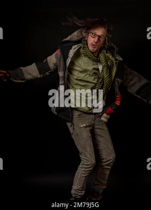 Uomo con pullover in lana colorata e pantaloni grigi con grandi stivali gialli e fondo nero Foto Stock