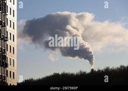 Pipa con fumo sopra il parco e l'edificio residenziale. Riscaldamento a gas o a carbone in inverno, concetto di inquinamento atmosferico Foto Stock