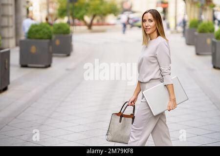 Elegante imprenditore femminile con netbook a passeggiare sulla strada cittadina Foto Stock