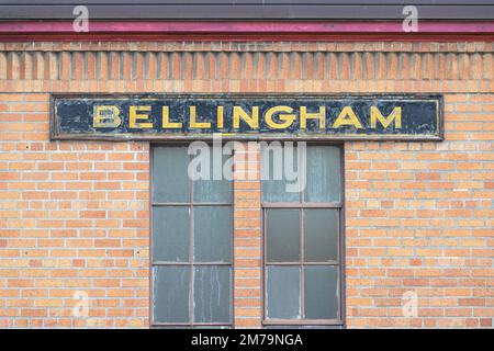 Bellingham, WA, USA - 5 gennaio 2023; vecchio cartello in legno per Bellingham montato su una parete di mattoni rossi sopra finestre opache Foto Stock