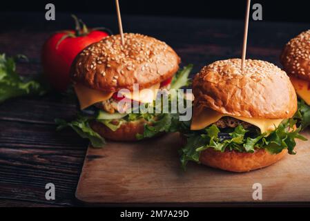 Succulenti hamburger fatti in casa con carne, formaggio, lattuga, pomodoro su un tavolo di legno Foto Stock