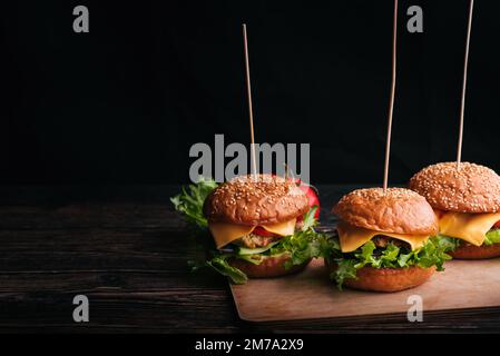 Tre hamburger fatti in casa con carne, formaggio, lattuga, pomodoro su una tavola di legno su sfondo nero con uno spazio per le copie Foto Stock