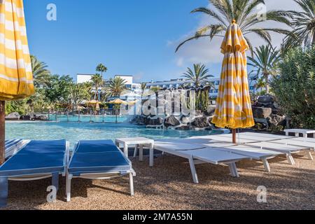 Puerto del Carmen, Spagna - 28 novembre 2022: Piscina con lettini, cascata artificiale, ombrelloni e piante tropicali native del Canar Foto Stock