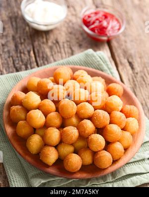 Patate duchessa fresche, tonde o crocchette su piatto di legno, ketchup e maionese sul retro (fuoco selettivo) Foto Stock