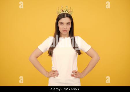 Giovane bella donna in corona su sfondo giallo. Ragazza con la corona regina che celebra la vittoria. Concetto del vincitore. Foto Stock