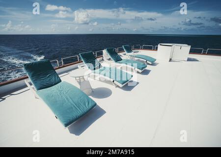 Una foto di quattro sedie a sdraio in fila con cuscini blu che le fiancheggiano sul ponte superiore di un lussuoso yacht da safari subacqueo che naviga intorno alle Maldive i. Foto Stock