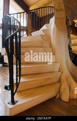 Scale in legno sbiancate con ringhiere in ferro battuto nero nel soggiorno all'interno di una lussuosa casa di legno. Foto Stock
