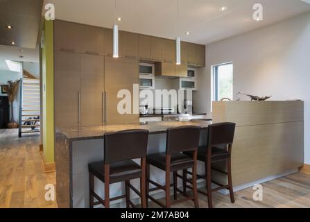 Isola con ripiano in granito grigio scuro e sedie da sgabello in pelle e legno con schienale alto in cucina all'interno di una casa moderna in stile cubista. Foto Stock