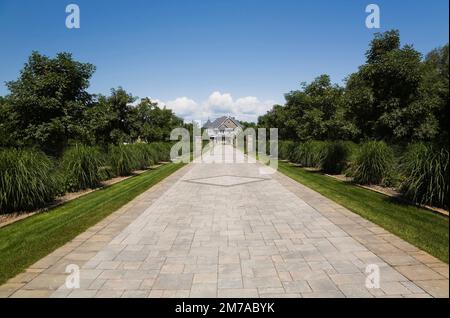 Vicolo in pietra con colonne in pietra delimitate da Miscanthus - piante ornamentali che conducono a un'elegante pietra grigia con finiture bianche e tetto blu. Foto Stock