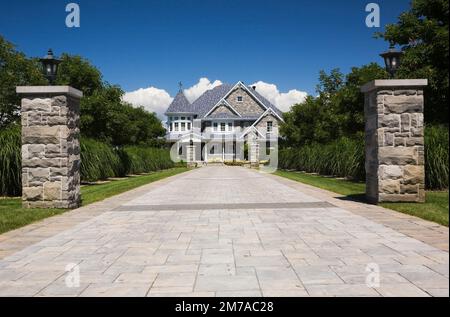 Viuzze di pietra con colonne di pietra delimitate da Miscanthus - piante ornamentali di erba che portano ad elegante pietra grigia con finiture bianche casa a due piani. Foto Stock