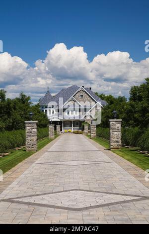 Vicolo in pietra con colonne in pietra delimitate da Miscanthus - piante ornamentali che conducono a un'elegante pietra grigia con finiture bianche e tetto blu. Foto Stock