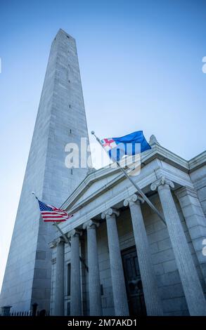 Il Monumento di Bunker Hill a Charlestown con obelisco e alloggio insieme alla bandiera degli Stati Uniti e alla bandiera del New England volò sul campo di battaglia di Breed's Hill Foto Stock