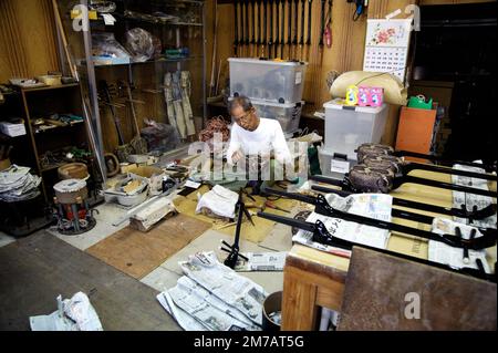Un artigiano che mette il tocco finale su un lotto di strumenti di 'sanshin'. Ho notato la scena e ho chiesto se potevo entrare per alcune foto. Foto Stock