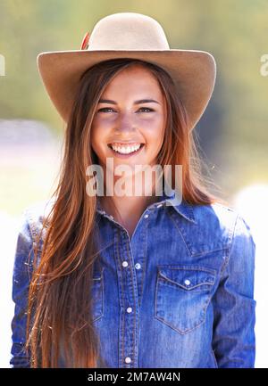 Possedere lo sguardo della cowgirl. Una giovane cowgirl attraente in piedi nelle stalle. Foto Stock