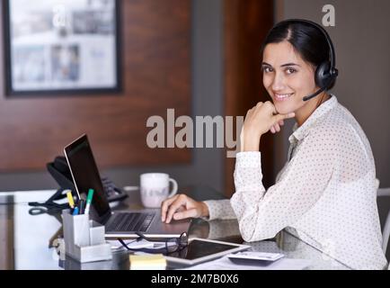 Shes sempre disponibile per rispondere alla chiamata. una giovane e attraente donna d'affari che lavora su un notebook indossando una cuffia. Foto Stock