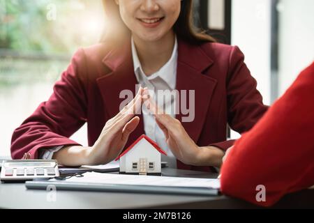 Concetto di bene immobile, Agente con una casa. Casa a portata di mano. Assicurazione e concetto di sicurezza della proprietà. Proteggere il gesto della donna e il simbolo della casa Foto Stock