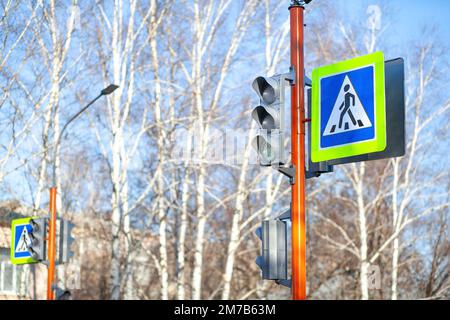 Sulla strada accanto alla scuola è presente un cartello di attraversamento pedonale con rivestimento riflettente e un semaforo che avverte i conducenti del pedone Foto Stock