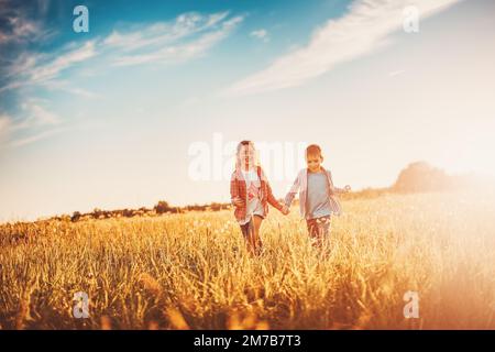 Due bambini corrono sul campo estivo tenendo le mani. Foto Stock