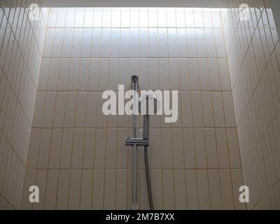 Doccia in acciaio inox con bar montato su pareti in piastrelle vintage, disegno verticale con sfondo giallo in boiacca nella moderna stanza da bagno dell'hotel. Foto Stock