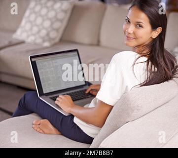 Ive ha tutto ciò di cui ho bisogno proprio qui. una giovane donna attraente seduta sul divano con il suo laptop. Foto Stock