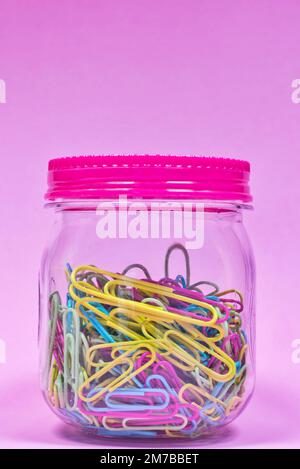 Graffette colorate in un vaso di vetro semplice e coperchio sigillato con sfondo rosa e spazio copia sopra, concetto creativo. Foto Stock