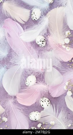 Sfondo pasquale con piume, uova e fiori di gypsofila bianca su carta violetta stropicciata. Giacitura piana, formato verticale Foto Stock