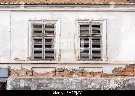 Facciata di un vecchio edificio in rovina con finestre in legno usurate con persiane Foto Stock