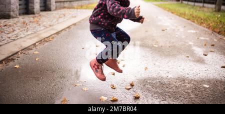 Un bambino salta sopra una pozza d'acqua e lascia - la strada sullo sfondo Foto Stock