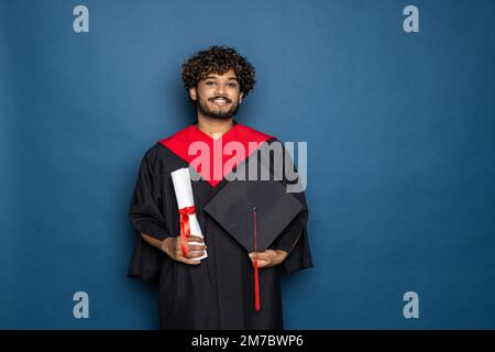 Istruzione, laurea e concetto di persone - felice indiano studente di laurea maschile in Mortarboard e abito da bachelor Foto Stock