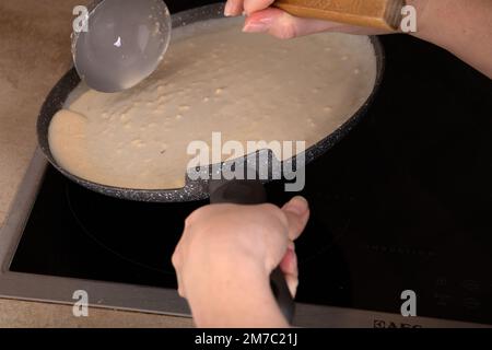 foto preparazione di frittelle sottili in una padella in cucina, le mani nella cornice Foto Stock