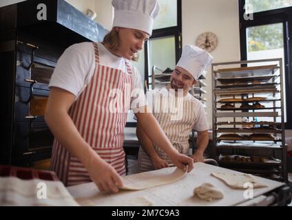 Uomo con giù sindromi aiutare a preabbinare il pane in panetteria con il suo collega. Concetto di integrazione delle persone con disabilità nella società. Foto Stock