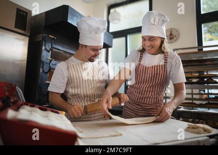 Uomo con giù sindromi aiutare a preabbinare il pane in panetteria con il suo collega. Concetto di integrazione delle persone con disabilità nella società. Foto Stock