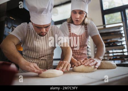 Uomo con giù sindromi aiutare a preabbinare il pane in panetteria con il suo collega. Concetto di integrazione delle persone con disabilità nella società. Foto Stock